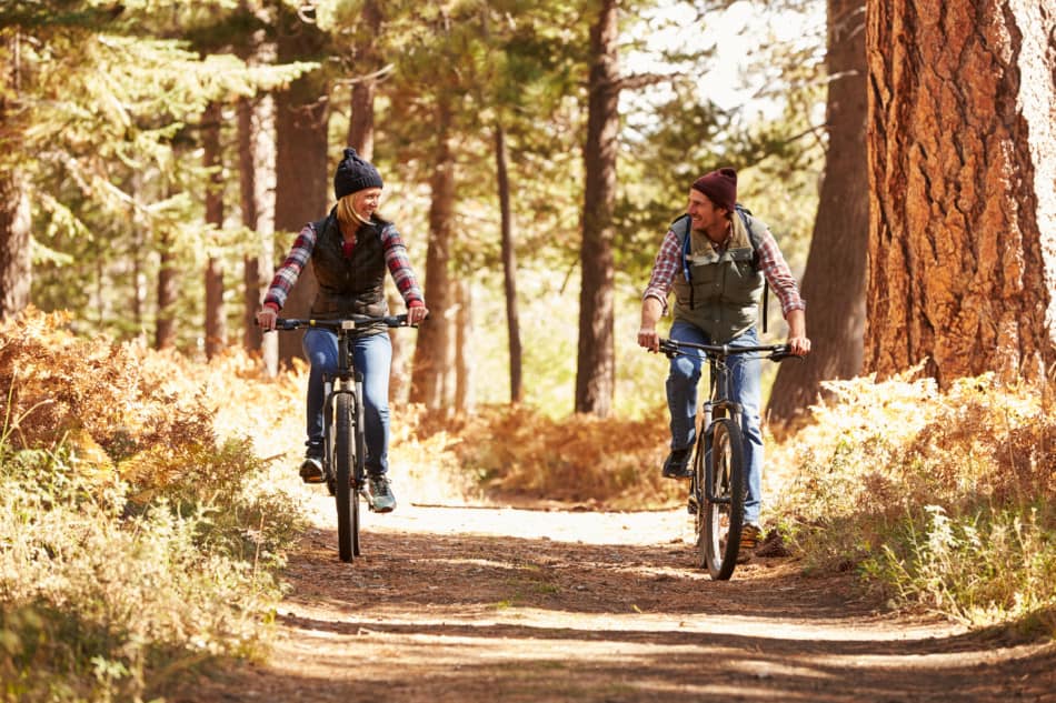 man and woman riding mountain bike on forest trail