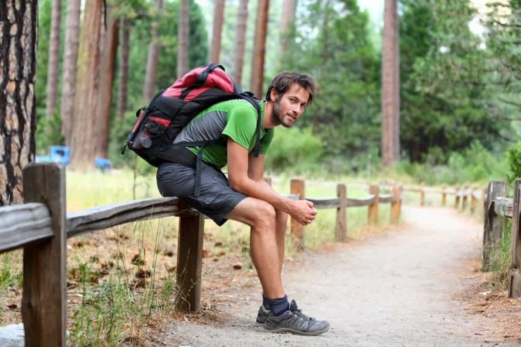 man wearing backpack resting on railing in park