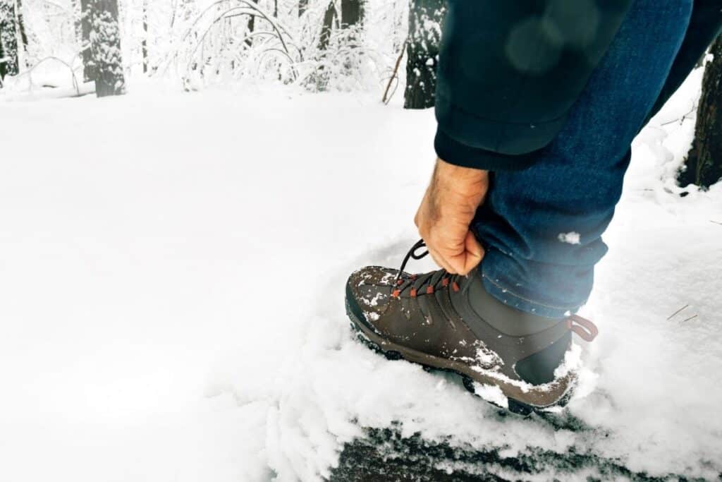 Many tying hiking shoe laces in snowy forest