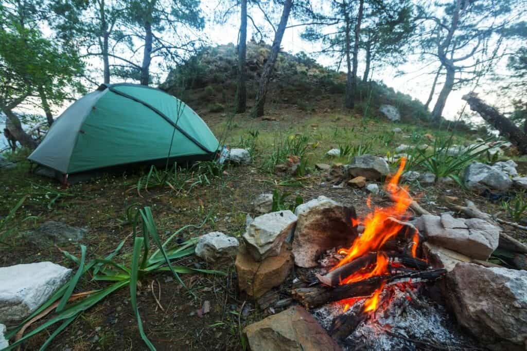 green tent in the woods by campfire