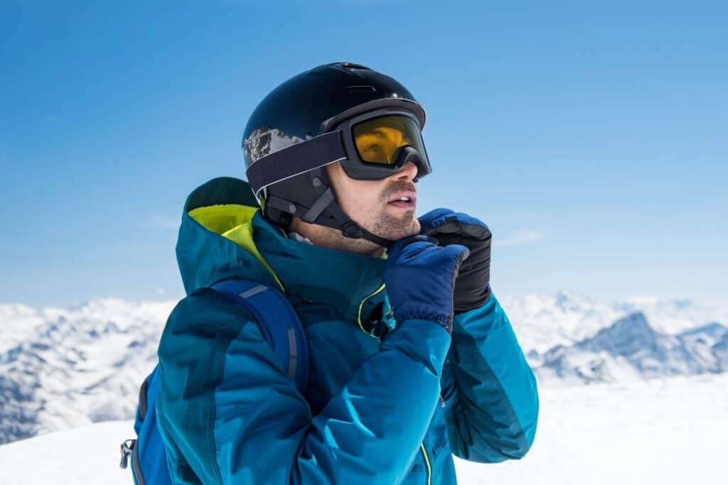 man attaching chin strap on ski helmet